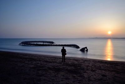 Person standing at beach by sculpture against clear sky