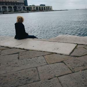 Rear view of woman sitting by sea against sky