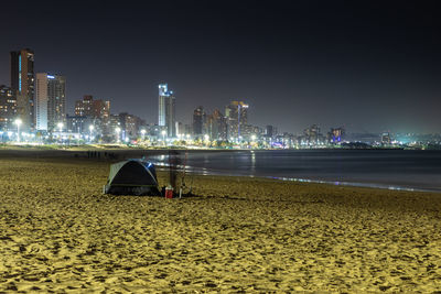 View of illuminated buildings at beach against sky