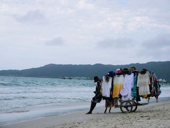 Man selling clothes at beach against sky