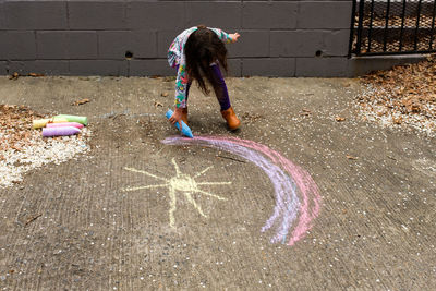 Little girl drawing rainbow with chalk