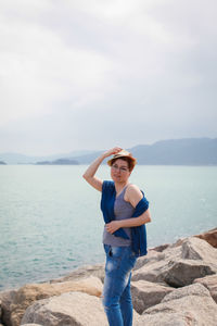 Portrait of woman standing on rocky shore against cloudy sky