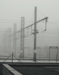 Electricity pylon by bridge against sky