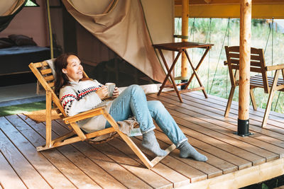 Brunette woman in nordic sweater drinking tea and relaxing in glamping in nature