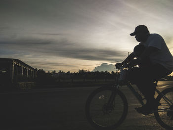 Man riding bicycle on road against sky during sunset
