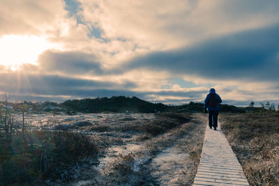 Rear view of woman walking on boardwalk at field during sunset