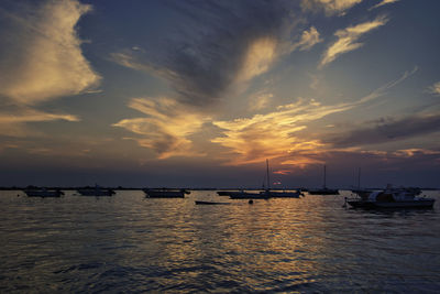 Sailboats moored on sea against sky at sunset