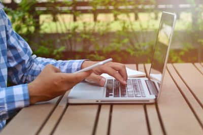 Midsection of man using laptop while holding mobile phone on table