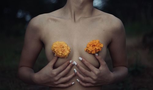 Midsection of naked woman holding flowers