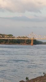 Bridge over calm sea against cloudy sky