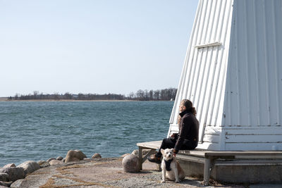 Woman sitting with dog on shore against clear sky