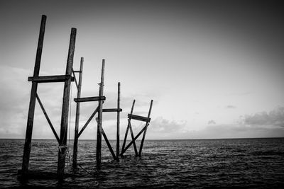 Wooden posts in sea against sky