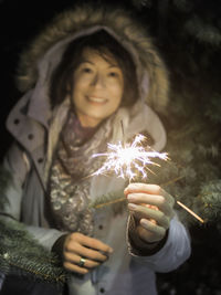 Portrait of woman holding sparkler at night