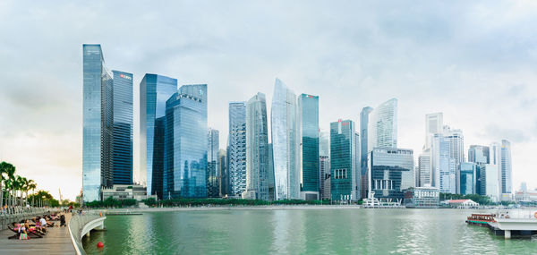 Modern buildings by river against sky in city