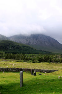 Green fields in front of mountains against cloudy sky