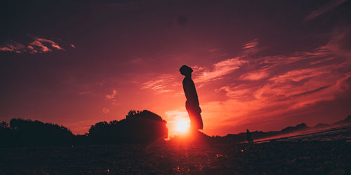 Silhouette person standing on field against sky during sunset