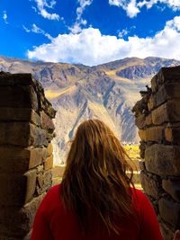 Rear view of woman looking at mountain while standing by brick wall