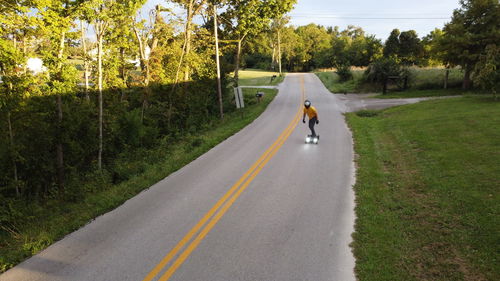 Man skateboarding down a country road.