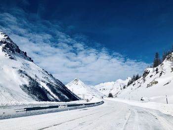 Snow covered road by snowcapped mountains against sky