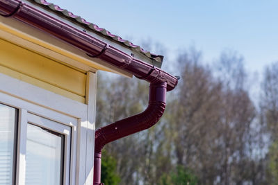 Corner of the house with gutter on a background of blue sky and spring forest