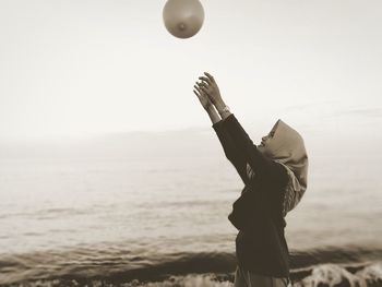 Side view of smiling mature woman playing with balloon in mid-air