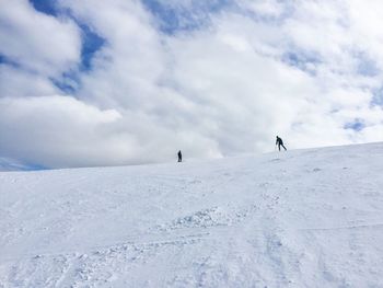 Low angle view of people skiing on snow covered landscape against cloudy sky