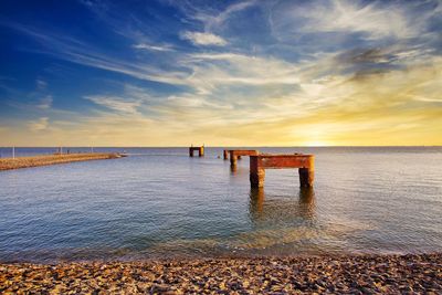 Wooden posts on beach against sky during sunset