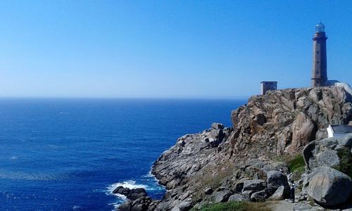 Lighthouse by sea against clear blue sky