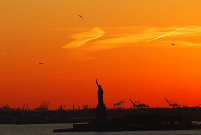 Silhouette of statue of liberty and liberty island in new york against an orange sunset sky