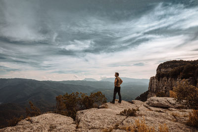 Man standing on rock looking at mountains against sky