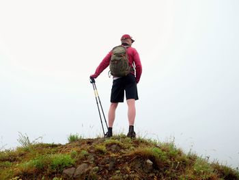 Man in cloud of fog. hiker in pink black sportswear and poles stand on mountain peak rock.