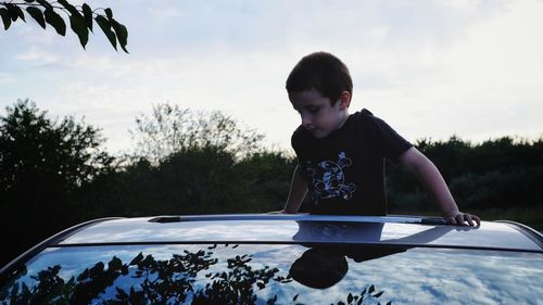 Boy standing and looking through car roof against sky