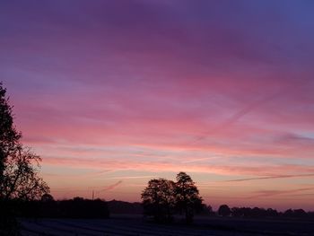 Silhouette trees on field against romantic sky at sunset