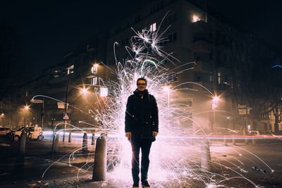 Smiling man standing against fire crackers on sidewalk in city at night