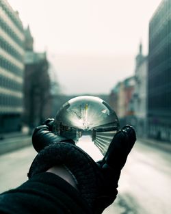 Close-up of hand holding crystal ball against city buildings