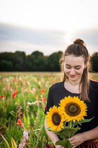 Portrait of young woman with sunflower standing on field