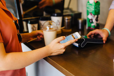 Midsection of woman using mobile phone to pay contactless at a local shop