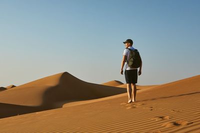 Rear view of man walking on sand dune in desert against clear sky