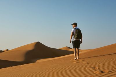 Man standing on sand dune in desert against clear sky