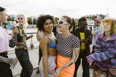 Portrait of smiling non-binary person celebrating with friends dancing on promenade in city