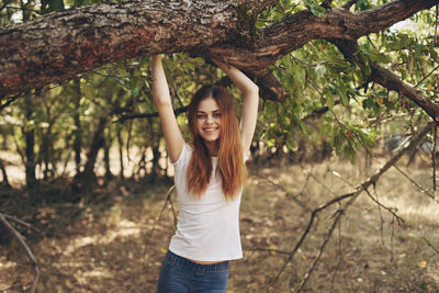 Portrait of young woman standing by tree trunk