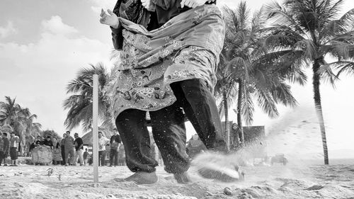 Low section of woman with palm trees on beach against sky