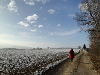 Rear view of woman walking on field against sky