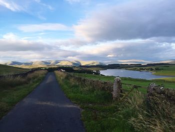 Empty road leading towards mountains against sky