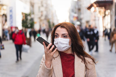 Woman wearing mask while using mobile phone while standing outdoors