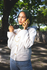 Portrait of beautiful young woman standing against trees