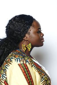 Side view of young curvy woman with afro hairstyle wearing colorful african shirt and earrings. she is looking away while standing on white wall background