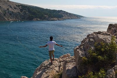 Rear view of man standing on rock by sea