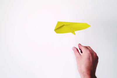 Cropped hand throwing paper airplane against white background