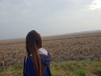 Rear view of woman standing on field against sky